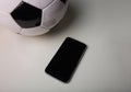 Live football betting concept, blank smartphone screen and classic soccer ball isolated on grey table minimalist background.