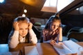 Live portrait of cute kids, sisters sitting at home doing homework with friend at evening time. Online education