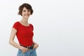 Lively attractive self-assured female trendy red t-shirt hold hands pockets stand profile turn camera smiling amused