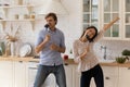 Lively attractive young couple singing dancing in kitchen