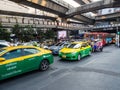 A bustling street in Bangkok, Thailand, with green and yellow taxis, buses, cars and a tuk-tuk under concrete fundaments of the