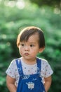 A lively little boy in blue overalls stands among the bushes in the park Royalty Free Stock Photo