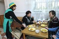 Living on a breadline. Social worker pouring soup in plate for poor old people sitting at a table of canteen Royalty Free Stock Photo