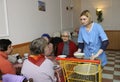 Living on a breadline. Social worker pouring soup in plate for poor old people sitting at a table of canteen