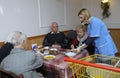 Living on a breadline. Woman social worker giving free meal to poor old people sitting at the table in canteen. Center Royalty Free Stock Photo