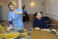 Living on a breadline. Woman social worker giving free meal to poor old people sitting at the table in canteen. Center Royalty Free Stock Photo