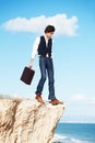 Living on the edge. Young semi-formal businessman stepping towards the edge of a cliff overlooking the ocean. Royalty Free Stock Photo