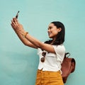 Living a life of colour. an attractive young woman standing and using her cellphone to take a selfie against a blue