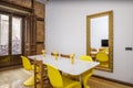 Living room with glossy white dining table with yellow resin chairs, gold framed mirror and brick wall with brown wooden balcony Royalty Free Stock Photo