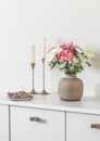 Living room interior - candles, fresh flowers in a ceramic vase, a notebook on a white chest of drawers in a bright scandinavian