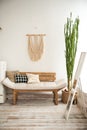 Living room with a rustic sofa. Sofa made of pallets, macrame on the wall, a large cactus in the room. Details of a light Scandina