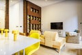 Living room of a vacation rental house decorated in yellow tones with a chaise longue sofa, white dining table and bookcase with Royalty Free Stock Photo