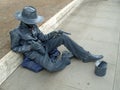A living statue of an Italian ganster sitting, asking for handout and keeping revolvers