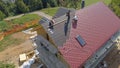 AERIAL: Workers lay red tin roofing sheets on a modern house under construction