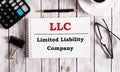 LLC Limited Liability Company is written in a white notepad near a calculator, coffee, glasses and a pen. Business concept