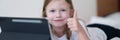 Llittle girl is lying on bed with tablet and holding thumbs up