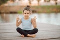 Llittle girl sitting in nature near by river or lake and practicing yoga. Healthy lifestyle