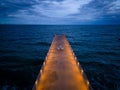 lluminated pier with dramatic sky over stormy dark sea at evening Royalty Free Stock Photo