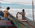 LoÃÂal fishermen stand on boat and untangle, range fishing net, in background ocean beach.