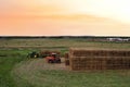 Loader at unload round bales of straw from hay trailer. Store hayat farm. Hay Forage feed for beef and dairy cattle. Making hay in