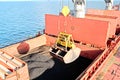 Loading coal from cargo barges onto a bulk carrier using ship cranes and grabs at the port of Samarinda, Indonesia.