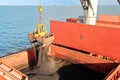 Loading coal from cargo barges onto a bulk carrier using ship cranes and grabs at the port of Samarinda, Indonesia. Royalty Free Stock Photo