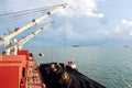 Loading coal from cargo barges onto a bulk carrier using ship cranes and grabs at the port of Samarinda, Indonesia.