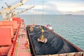 Loading coal from cargo barges onto a bulk carrier using ship cranes and grabs at the port of Samarinda, Indonesia. Royalty Free Stock Photo