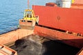 Loading coal from cargo barges onto a bulk carrier using ship cranes and grabs at the port of Samarinda, Indonesia. Royalty Free Stock Photo