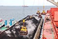 Loading coal from cargo barges onto a bulk carrier using ship cranes and grabs at the port of Samarinda, Indonesia.