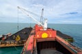 Loading coal from cargo barges onto a bulk vessel using ship cranes.