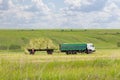 Loading hay rolls into an agricultural truck trailer. Preparation of feed for farm animals, haymaking