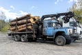 Loading heavy industrial truck trailer with big timber pine, spruce, cedar logs by crane grab loader tractor machine Royalty Free Stock Photo