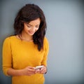 Loading her phone with new apps. Studio shot of a young woman using her phone against a gray background.