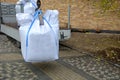 Loading large white plastic bags full of roofing substrate onto a smaller truck. crane holding in the air a cubic meter of heavy g