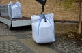 Loading large white plastic bags full of roofing substrate onto a smaller truck. crane holding in the air a cubic meter of heavy g