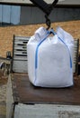 Loading large white plastic bags full of roofing substrate onto a smaller truck. crane holding in the air a cubic meter of heavy g