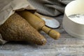 A loaf of bread along with rocking for the dough in a craft bag stand on a wooden table, next to it is satiated with flour. Top