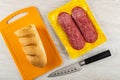 Loaf of bread on cutting board, slices of sausage salami in vacuum package, knife on wooden table. Top view Royalty Free Stock Photo