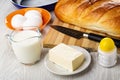 Loaf of bread, knife on cutting board, salt, frying pan, butter in saucer, eggs in bowl, jug of milk on table Royalty Free Stock Photo