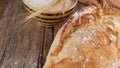 Loaf of bread on a wooden table, in the background a bowl of flour and spikelets of wheat