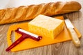 Loaf of bread, piece of marble cheese, cheese cutter, knife on cutting board on wooden table Royalty Free Stock Photo