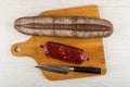 Loaf of bread, sausage in polyethylene pack, knife on cutting board on wooden table. Top view Royalty Free Stock Photo