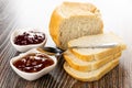 Loaf of bread, slices of bread, spoon, bowls with jam on wooden table