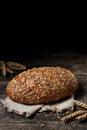 Loaf of brown bread with sesame and linseeds on textile towel on black wooden background with copy space