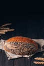 Loaf of brown bread with sesame and poppy seeds on textile towel on black wooden background with copy space Royalty Free Stock Photo