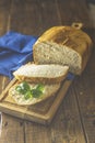 Loaf of freshly baked bread with basil and bread slices on wooden board over rustic wooden table background. Shallow depth of Royalty Free Stock Photo