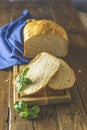 Loaf of freshly baked bread with basil and bread slices on wooden board over rustic wooden table background. Shallow depth of Royalty Free Stock Photo