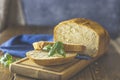 Loaf of freshly baked bread with basil and bread slices on wooden board over rustic wooden table background. Shallow depth of Royalty Free Stock Photo