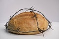 A loaf of round wheat bread wrapped with barbed wire, white background. The concept of food crisis, food shortage. Royalty Free Stock Photo